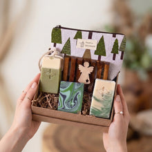 Load image into Gallery viewer, Vegan bath and body gift set with three handcrafted soaps, wooden soap dish, seasonal tree-print pouch and a wooden angel. Packed in crinkle paper and kraft box.