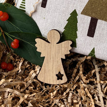 Load image into Gallery viewer, Small wooden angel ornament with a star-shaped cutout at the base, placed on crinkle paper next to a fabric pouch with green tree print.