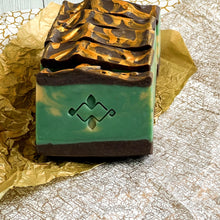 Charger l&#39;image dans la galerie, Five artisan soap bars with a carved golden swirl tops, rich green core, and dark chocolate base. The front face features an embossed geometric logo, representing handcrafted cold process soap for natural skincare routines.