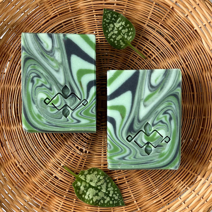 Two herbal sage soap bars lying side-by-side, with marbled green and black swirls and visible hand-carved Woods and Mosses logo imprint on each.