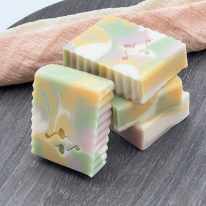 Pastel handmade soap bar with soft swirl colors, vegan and natural, placed on textured background.