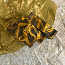 Charger l&#39;image dans la galerie, Top-down view of three handmade soap bars arranged side by side, showing dark chocolate tops with bold golden swirl patterns. Decorative texture highlights cold process craftsmanship for natural soap and artisan skincare.