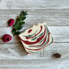 Load image into Gallery viewer, A square soap bar with the Woods and Mosses company logo in the middle. It is white with red and green swirls. 