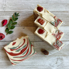 Load image into Gallery viewer, A square soap bar with the Woods and Mosses company logo in the middle. It is white with red and green swirls. The top is textured and decorated with red gemstones and glitter.